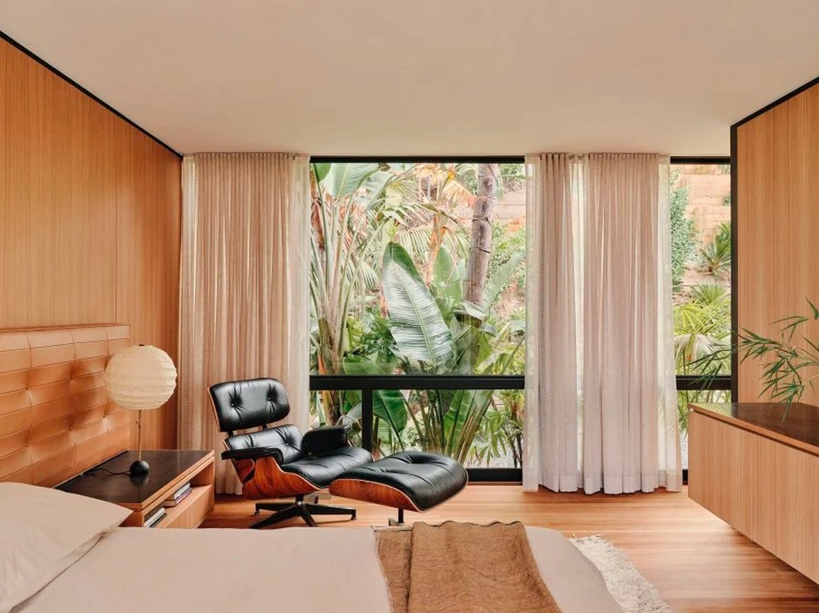 Thiết kế phòng ngủ ấm cúng với sàn và tường ốp gỗ teak, kết hợp cây xanh và khung cửa sổ đen tại nhà Moore để có phòng ngủ ấm cúng