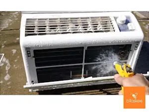Người kỹ thuật đang sử dụng vòi xịt nước để làm sạch bụi bẩn bám trên dàn lá tản nhiệt của cục nóng máy lạnh ngoài trời.
